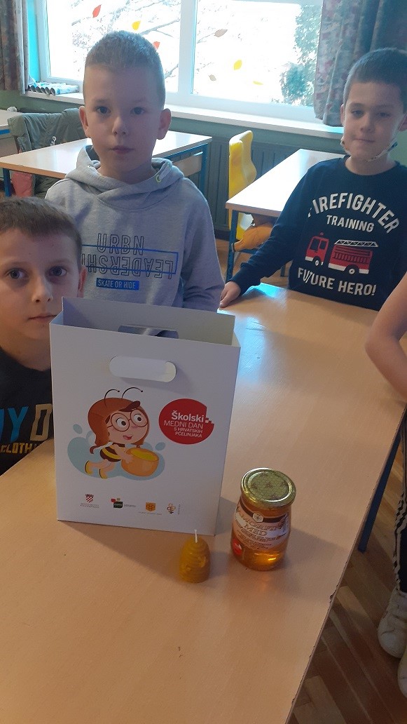 djeca sjede oko stola na kojem je staklenka meda